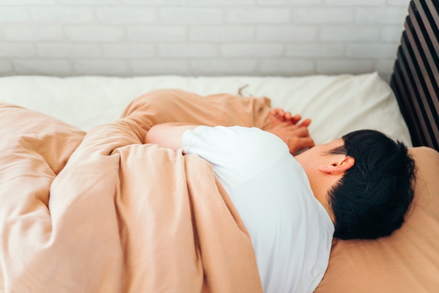 ベットで横向きに寝る男性