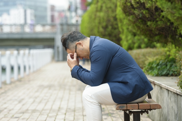 ベンチの座って頭を抱える男性