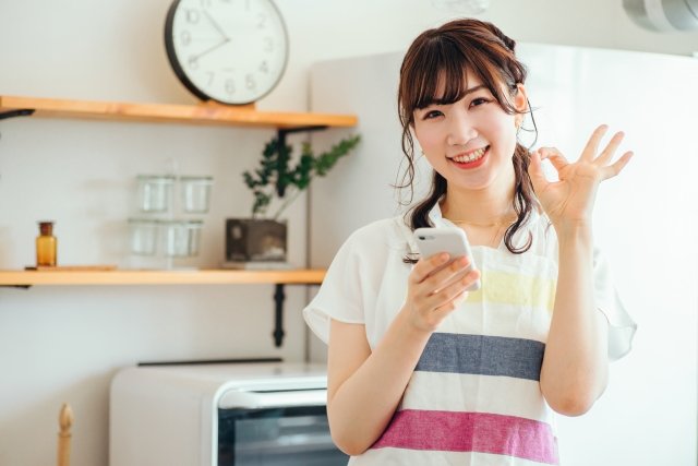 キッチンでスマホを持った笑顔の女性